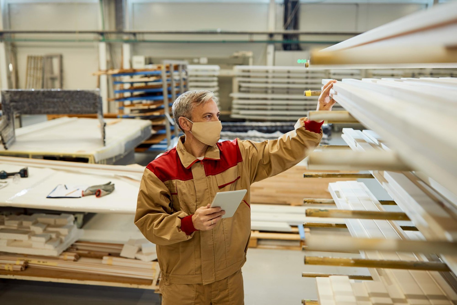 A skilled inspector, wearing a protective mask and work uniform, meticulously examines a rack of finished furniture components, holding a digital tablet to record observations. This highlights the "What to Check Before You Buy or Accept Delivery" aspect of quality control in furniture manufacturing.